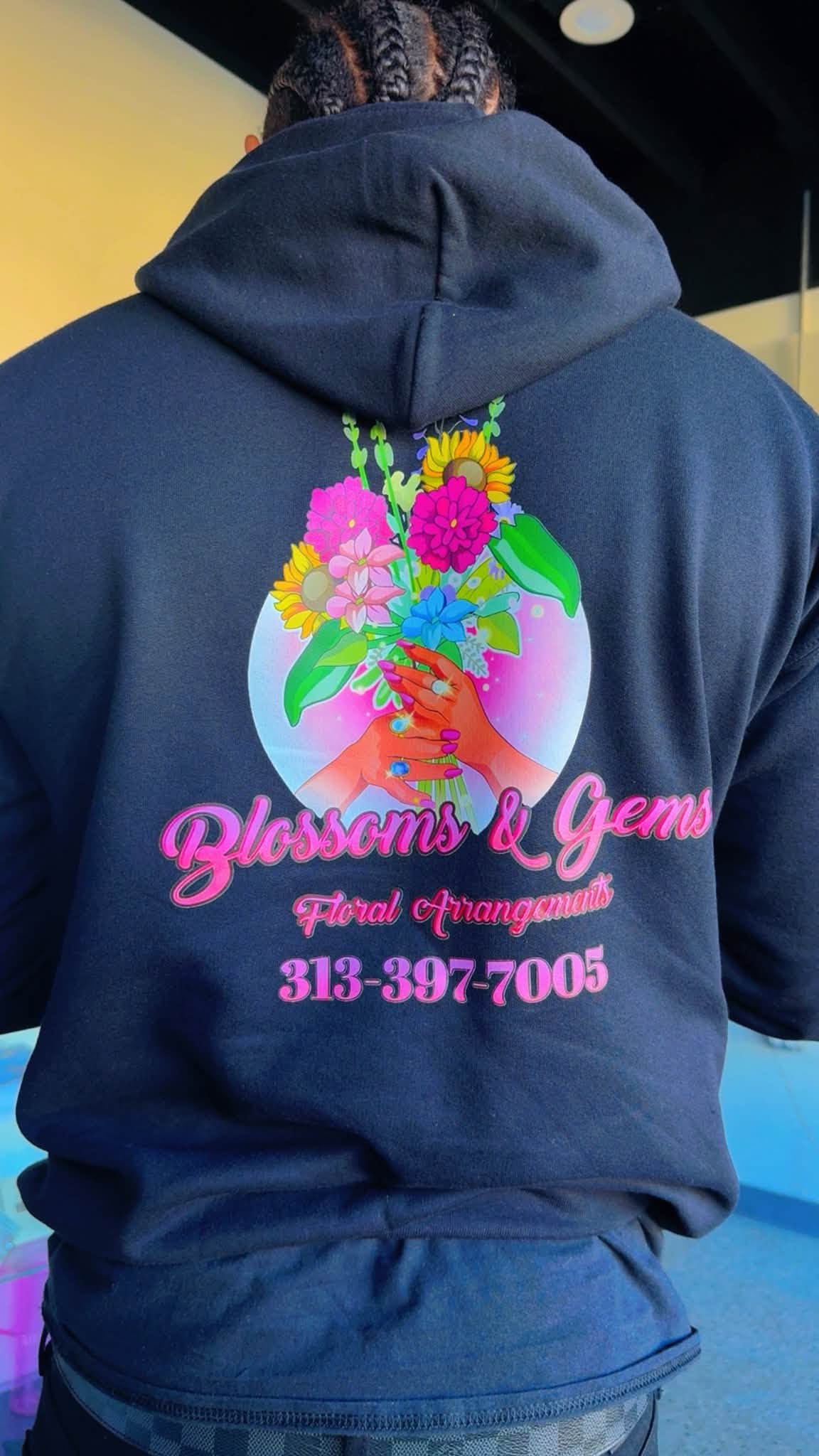 Blossoms & Gems logo printed on the back of a shop hoodie, with the shop phone number