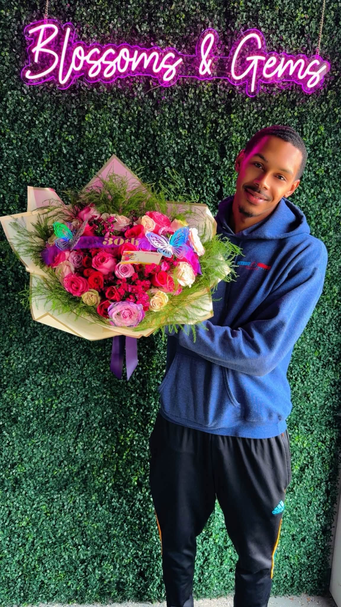 A customer holding a large wrapped bouquet at the shop's pink neon sign wall