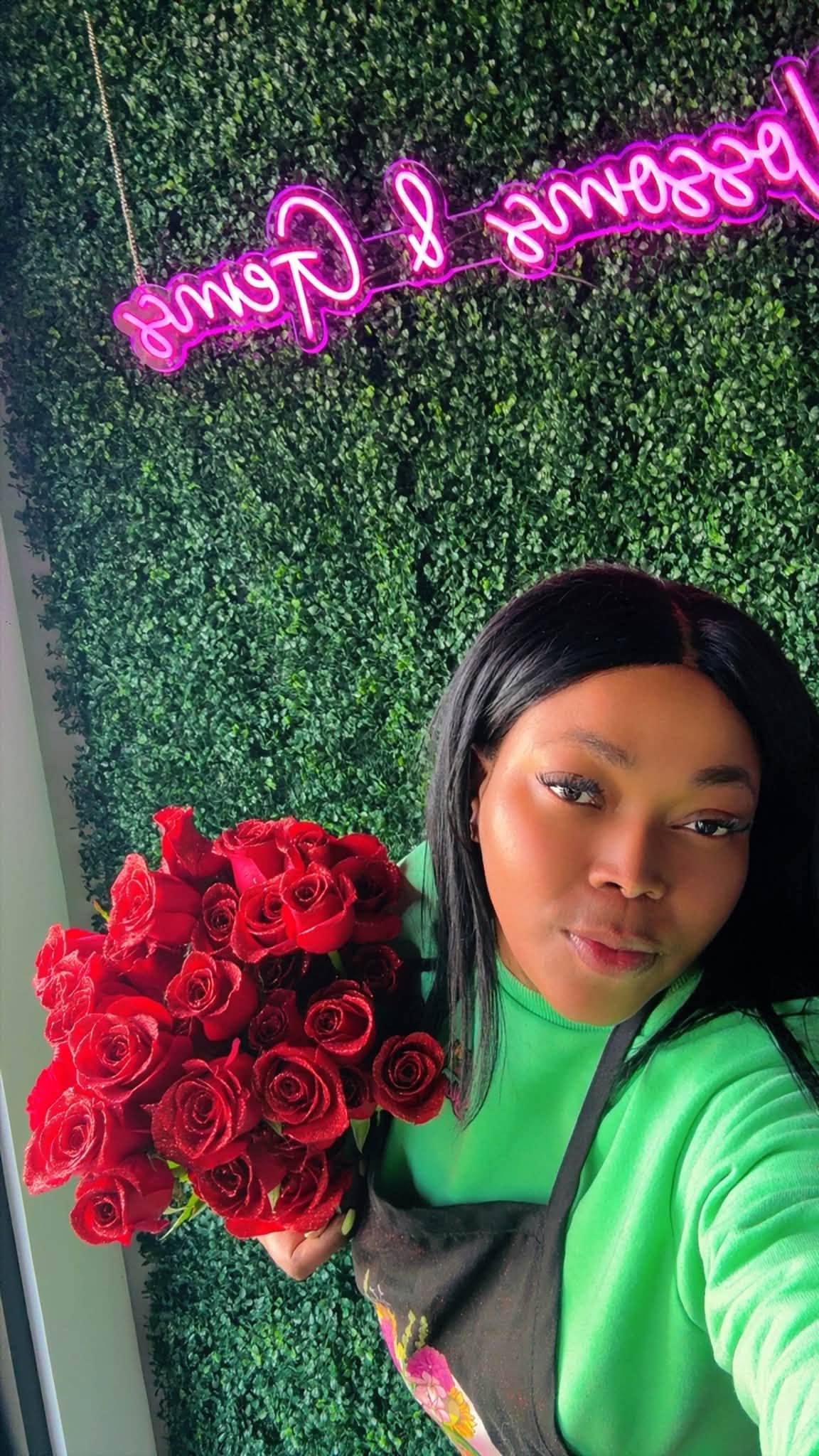 Inside Blossoms & Gems — holding a red rose bouquet in front of the shop's pink neon sign